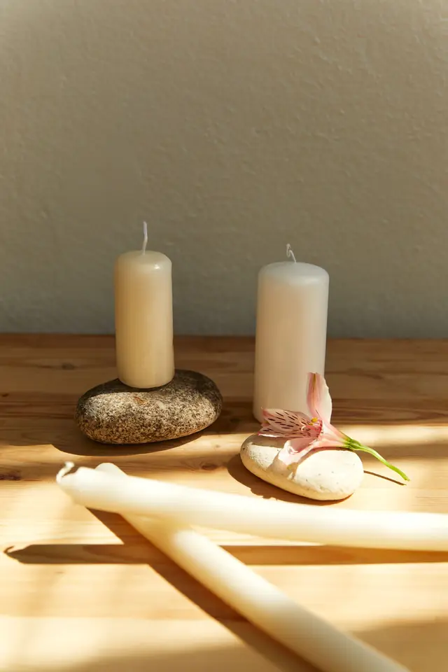 Bougies blanches posées sur des galets, sur une table en bois clair